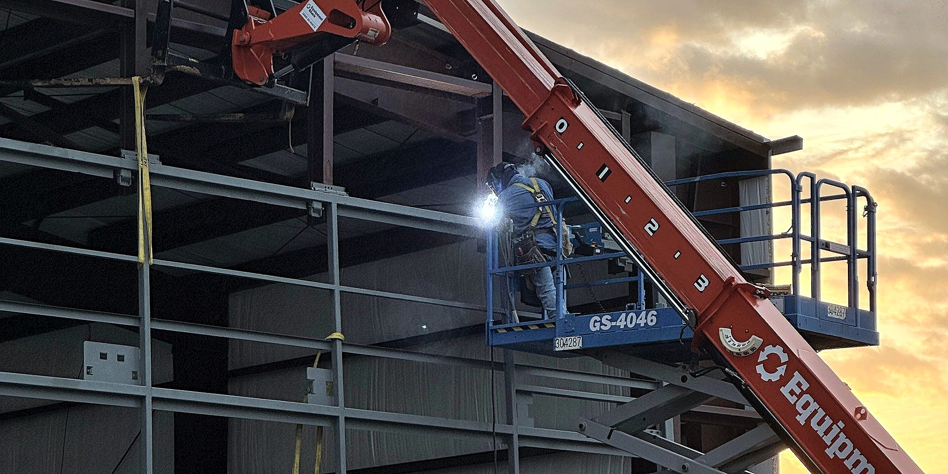 Welder working from a lift on a steel building at sunrise