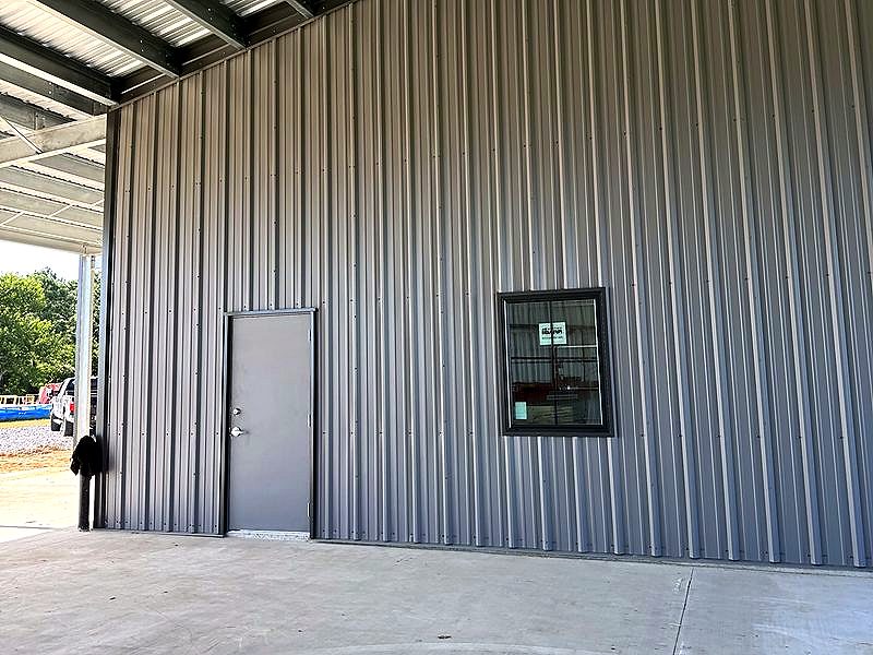 Finished metal building wall with a door and window under a covered canopy