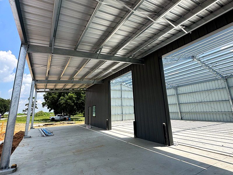 Covered canopy on galvanized columns beside large bay openings in a metal building