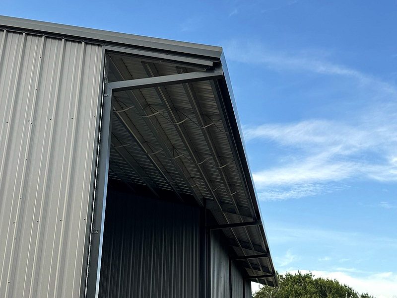 Corner of a gray metal building with a covered canopy against a blue sky