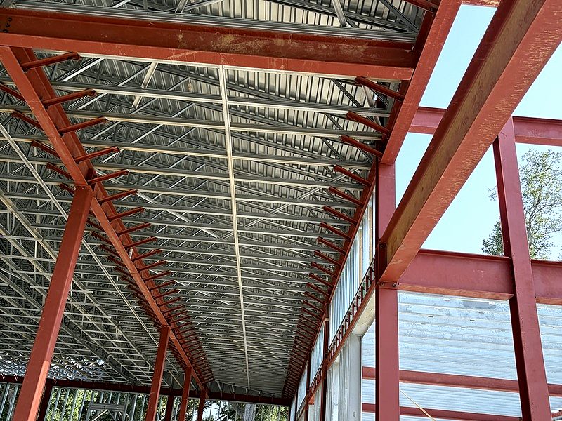 Looking up at red-iron beams and light-gauge steel roof trusses with scissor lifts below