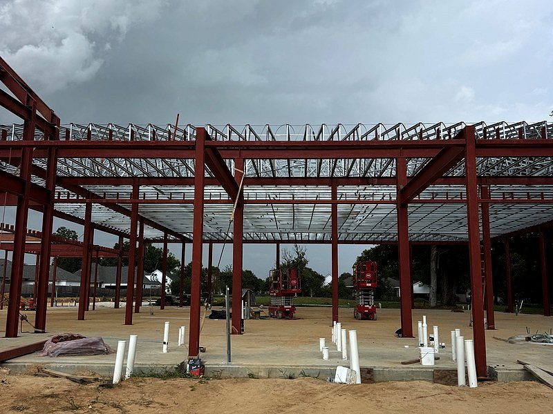 Red-iron structural steel frame with light-gauge roof trusses under storm clouds