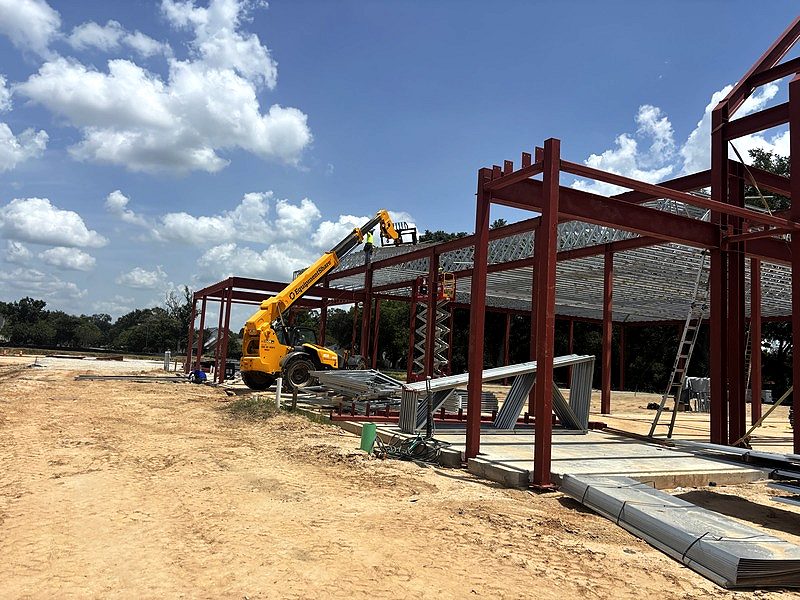 Telehandler lifting light-gauge steel trusses onto a red-iron frame
