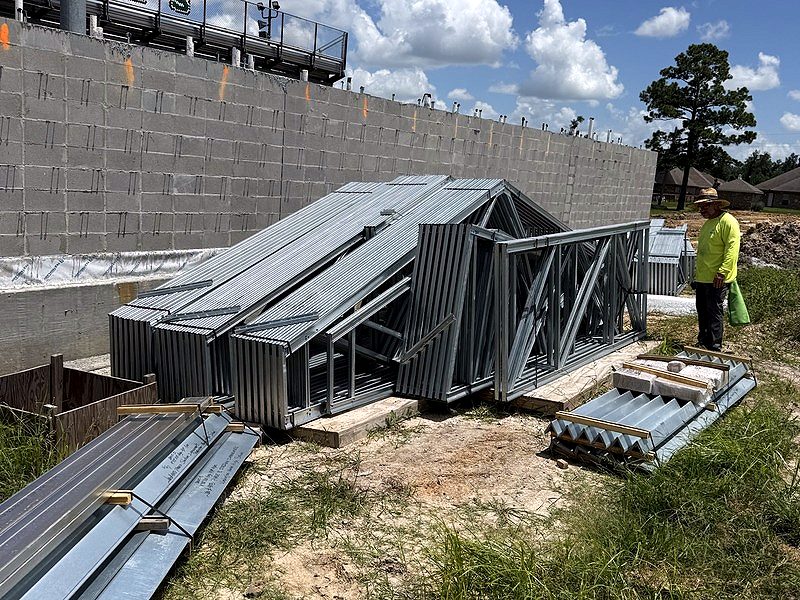 Bundles of light-gauge steel trusses staged beside a block wall at a stadium
