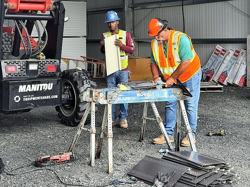 Two crew members cutting soffit panels inside a building
