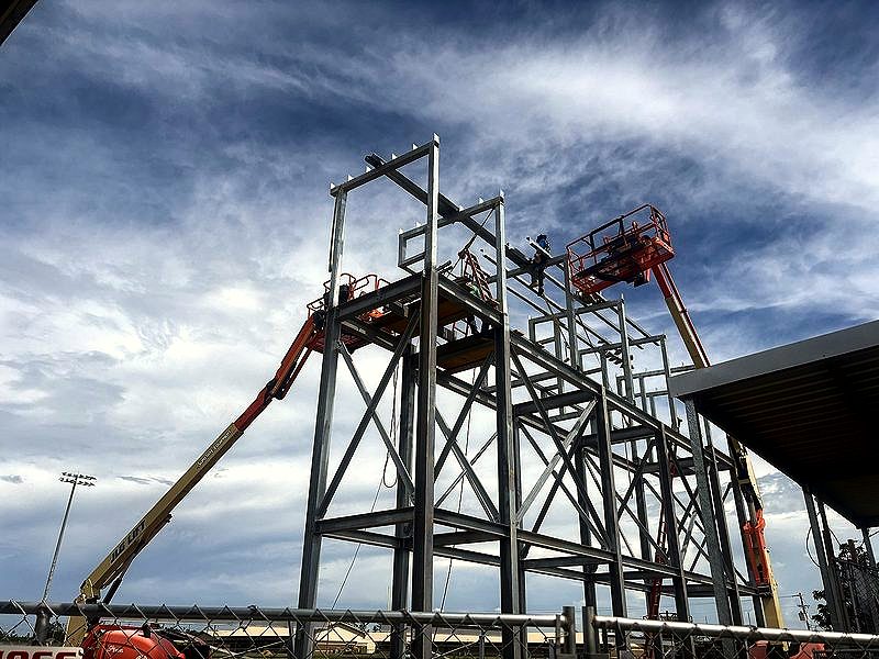 Structural steel tower with boom lifts against a cloudy sky