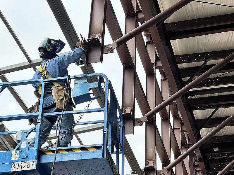 Ironworker on a blue lift connecting roof steel