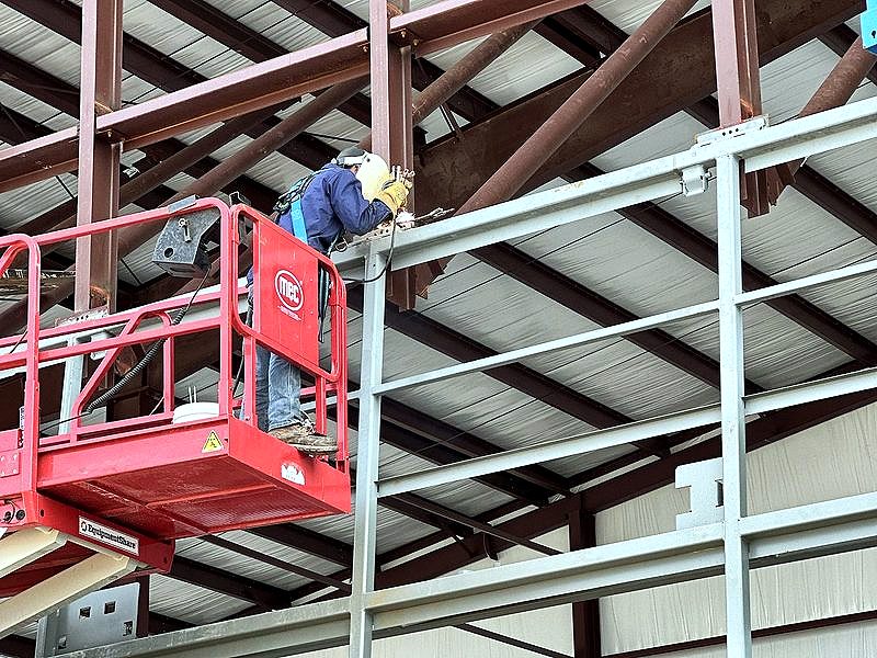 Welder on a red scissor lift working on steel framing