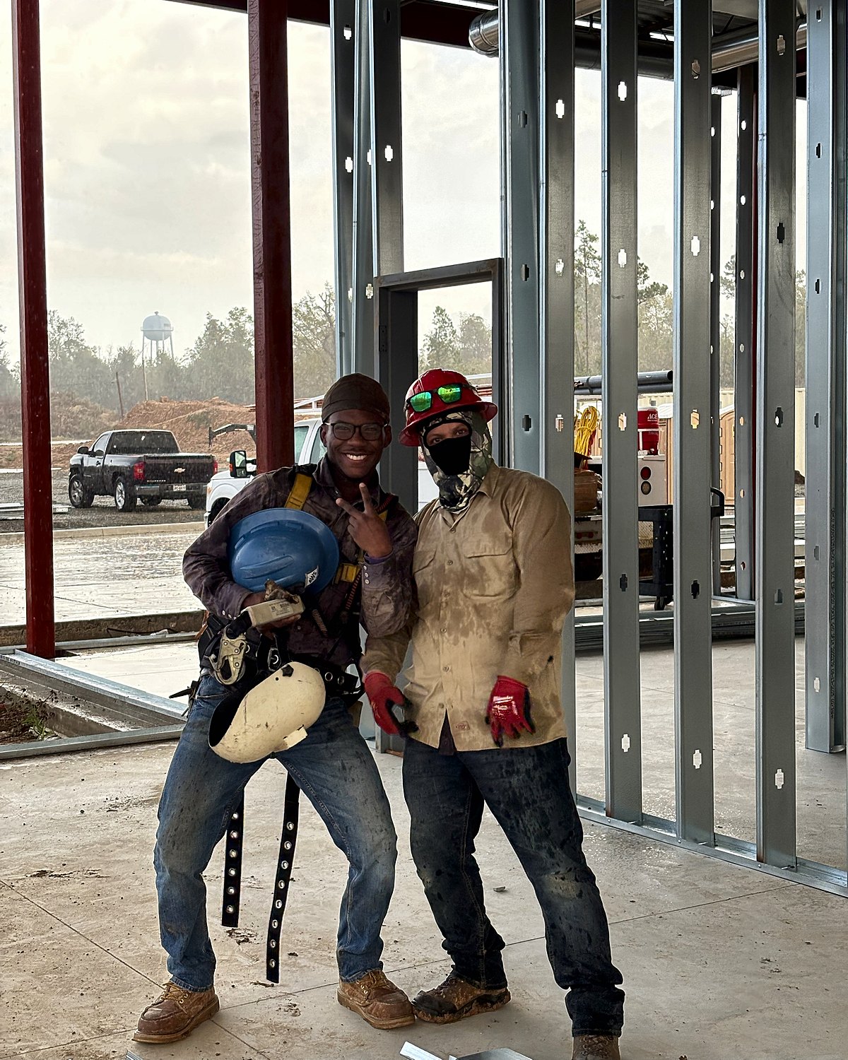 Two crew members smiling on a job site inside a steel-framed building