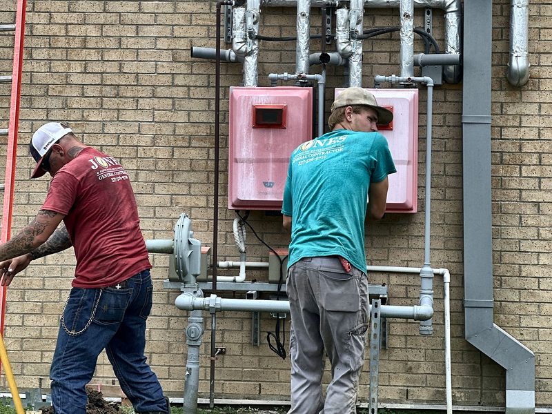 Two crew members installing tankless water heaters on a brick wall