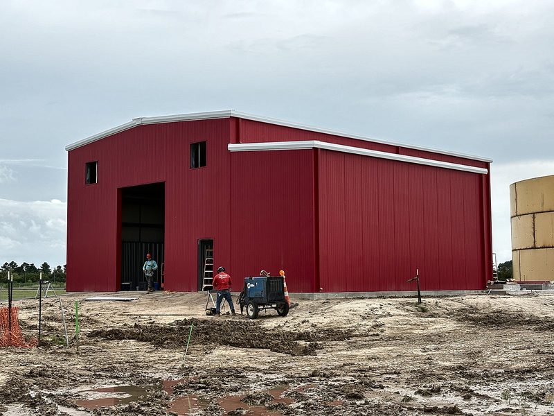 Red pre-engineered metal building with crew working out front
